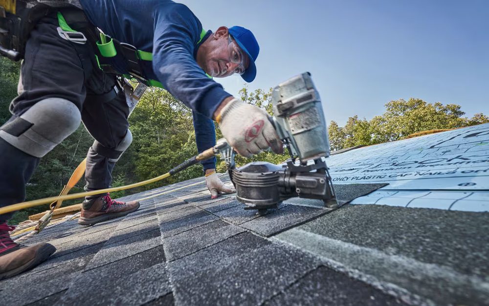 Roofer fastening architectural shingles with a nail gun